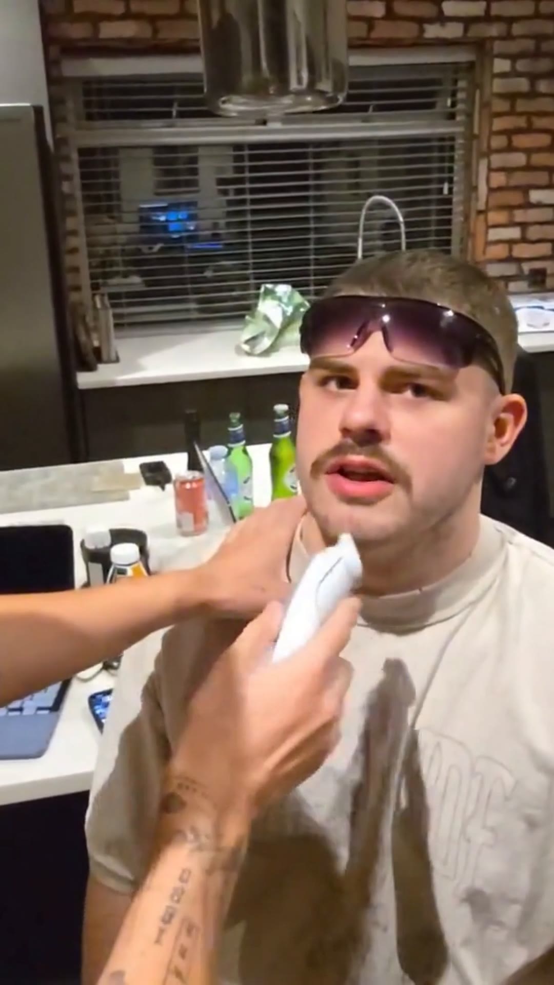 Vertical frame from the clip: Kobez in his kitchen, sunglasses on his head, with a beard trimmer at his chin
